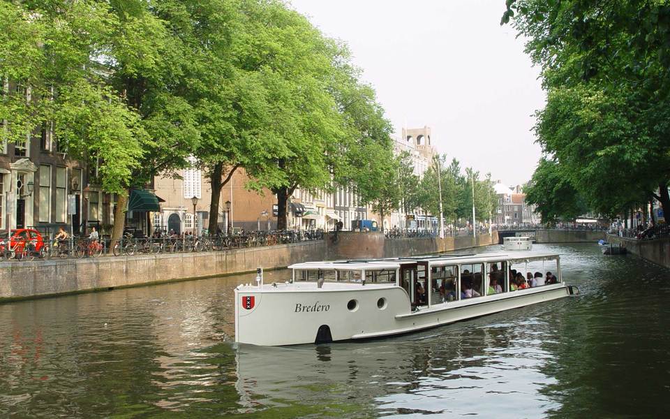 Strak wit motorjacht dat onder een grachtenbrug in Amsterdam vaart